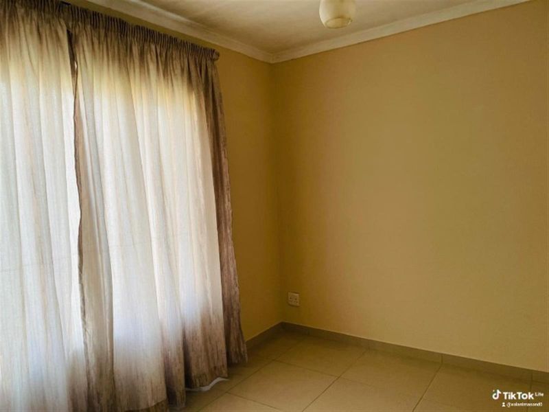 A simple, empty bedroom featuring neutral wall paint, tiled flooring, and installed curtain tracks, providing a blank canvas for personalization.
