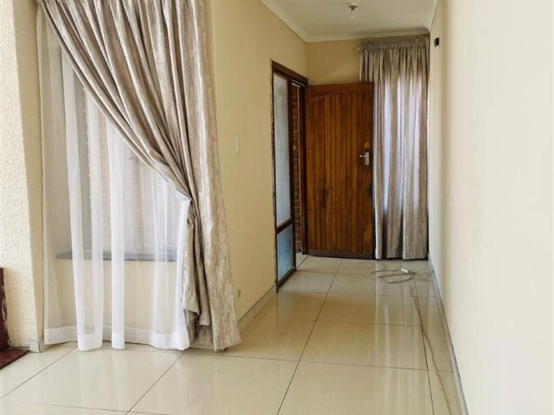 A bright, empty hallway featuring neutral tiled flooring, a timber entrance door, and simple window treatments.