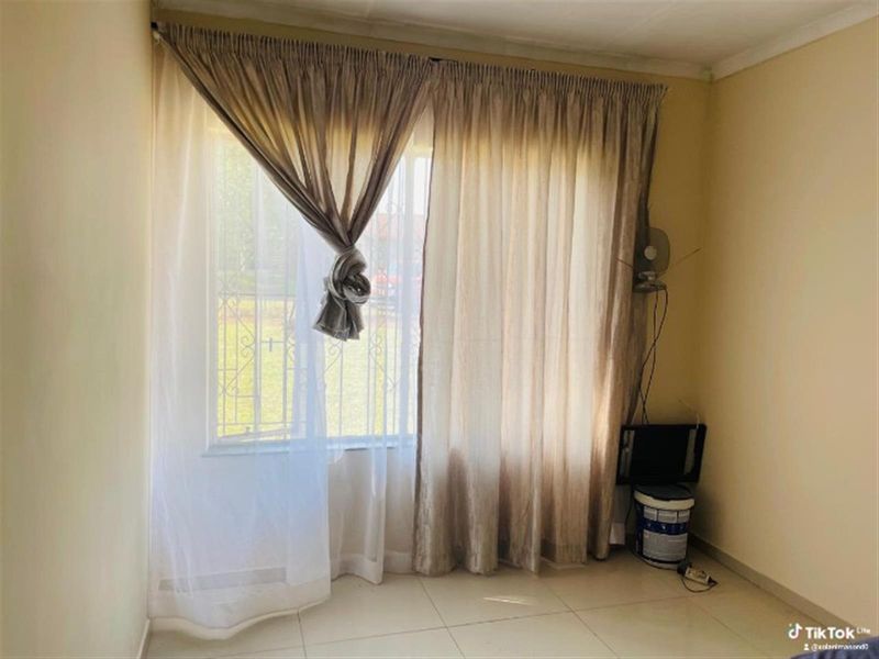 A simple, empty bedroom featuring tiled flooring and security bars on the window, providing a blank canvas for potential interior design updates.