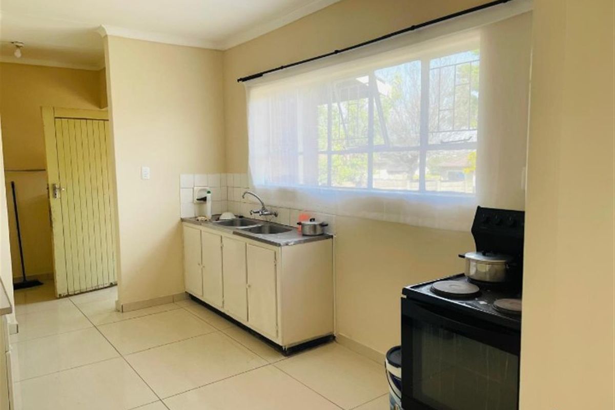 A functional kitchen featuring tiled flooring, a stainless steel double sink, and built-in cabinetry with a tiled splashback.