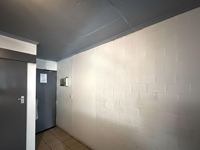 A functional hallway featuring tiled flooring, a painted brick feature wall, and a secure entrance door with an integrated intercom system.