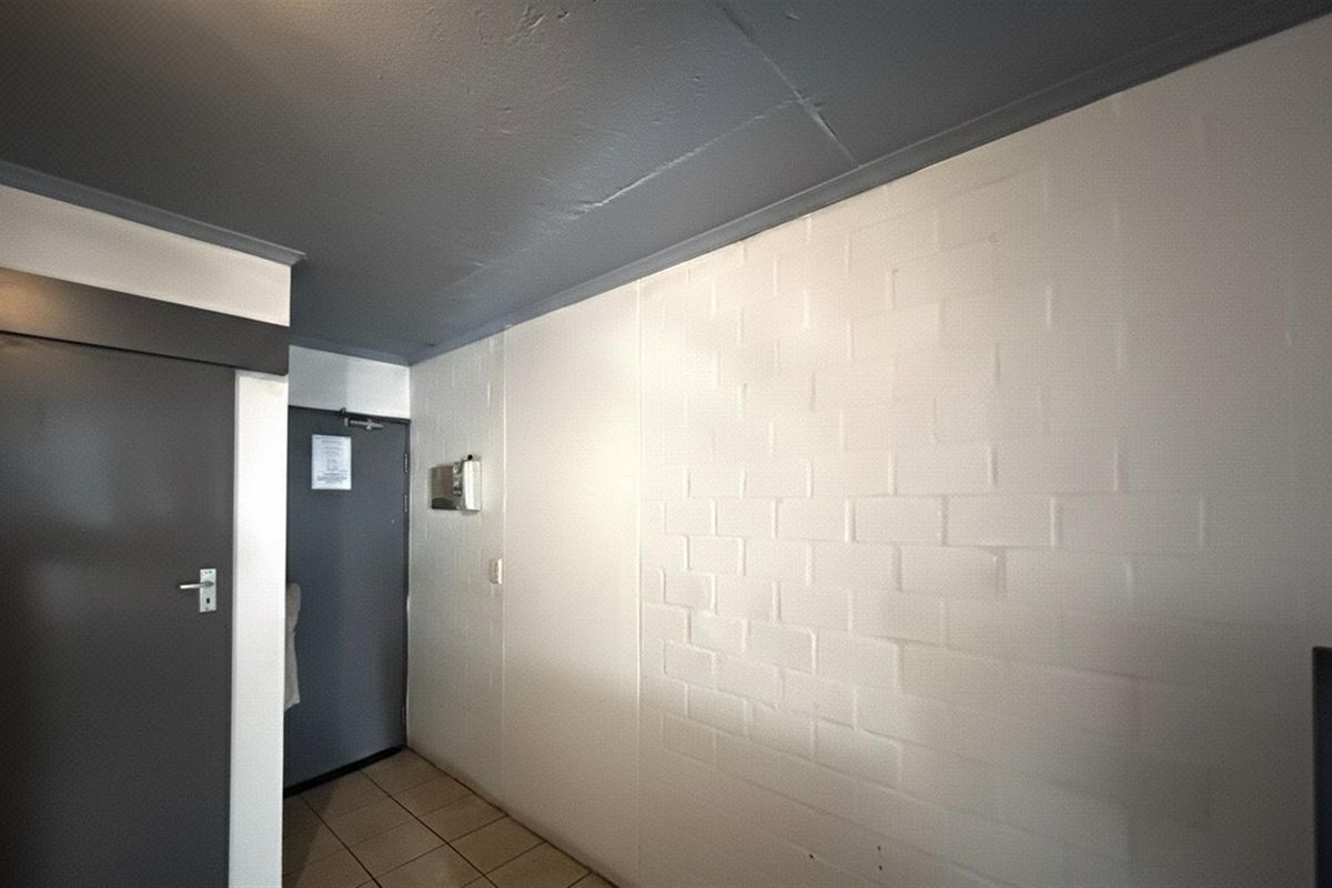 A functional hallway featuring tiled flooring, a painted brick feature wall, and a secure entrance door with an integrated intercom system.