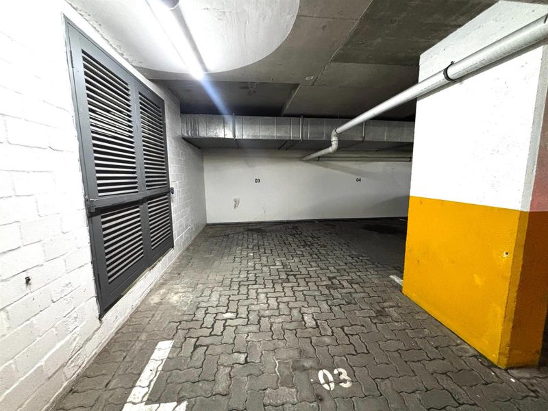 A covered parking bay featuring paved flooring, exposed ventilation ducting, and a louvered shutter window.