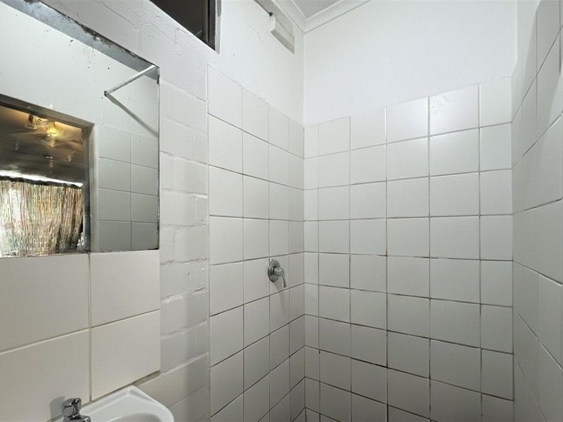 A functional bathroom featuring a tiled shower enclosure, pedestal basin, and wall-mounted mirror, requiring cosmetic updates to refresh the dated finishes.