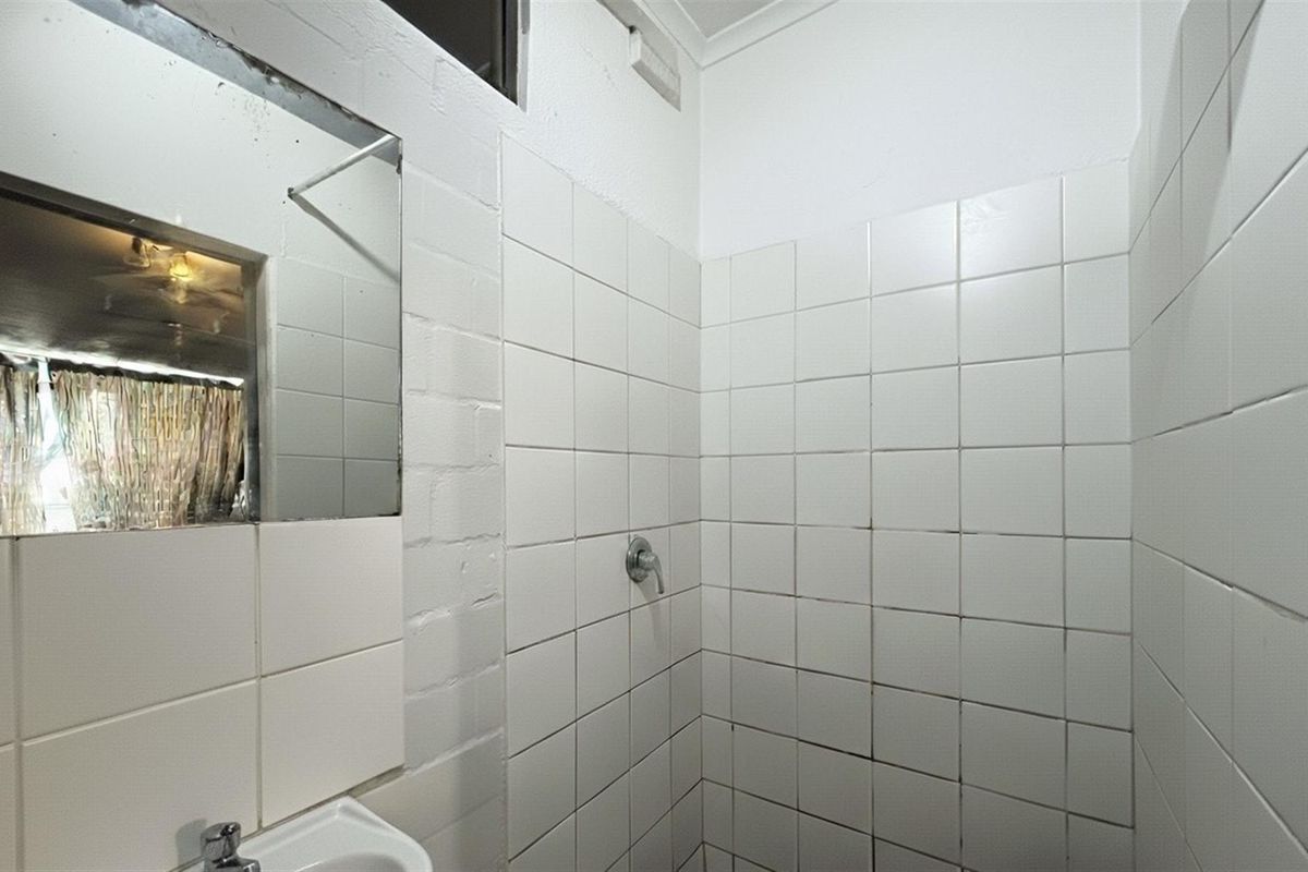 A functional bathroom featuring a tiled shower enclosure, pedestal basin, and wall-mounted mirror, requiring cosmetic updates to refresh the dated finishes.