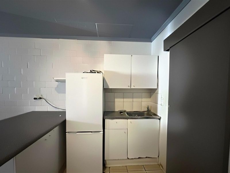 A compact kitchen area featuring basic built-in cabinetry, a stainless steel sink, and tiled splashback, requiring cosmetic updates to improve functionality and aesthetic appeal.