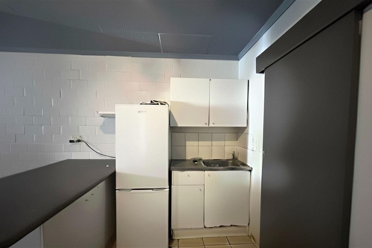 A compact kitchen area featuring basic built-in cabinetry, a stainless steel sink, and tiled splashback, requiring cosmetic updates to improve functionality and aesthetic appeal.