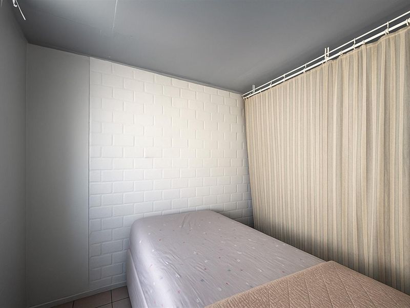 A compact bedroom featuring a white painted brick accent wall and neutral ceiling finishes.