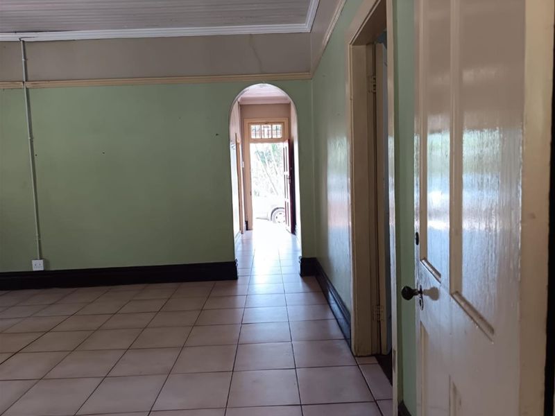 An empty hallway featuring tiled flooring, an arched transition, and traditional panelled doors, leading towards an exterior entrance.