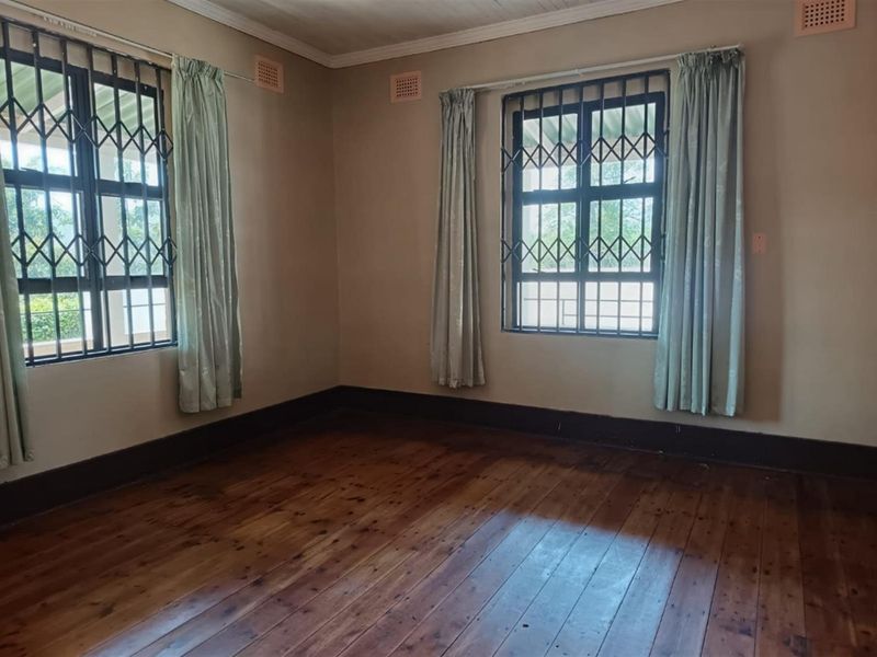 An empty bedroom featuring original timber flooring, security bars on windows, and a classic timber ceiling, offering a blank canvas for renovation.