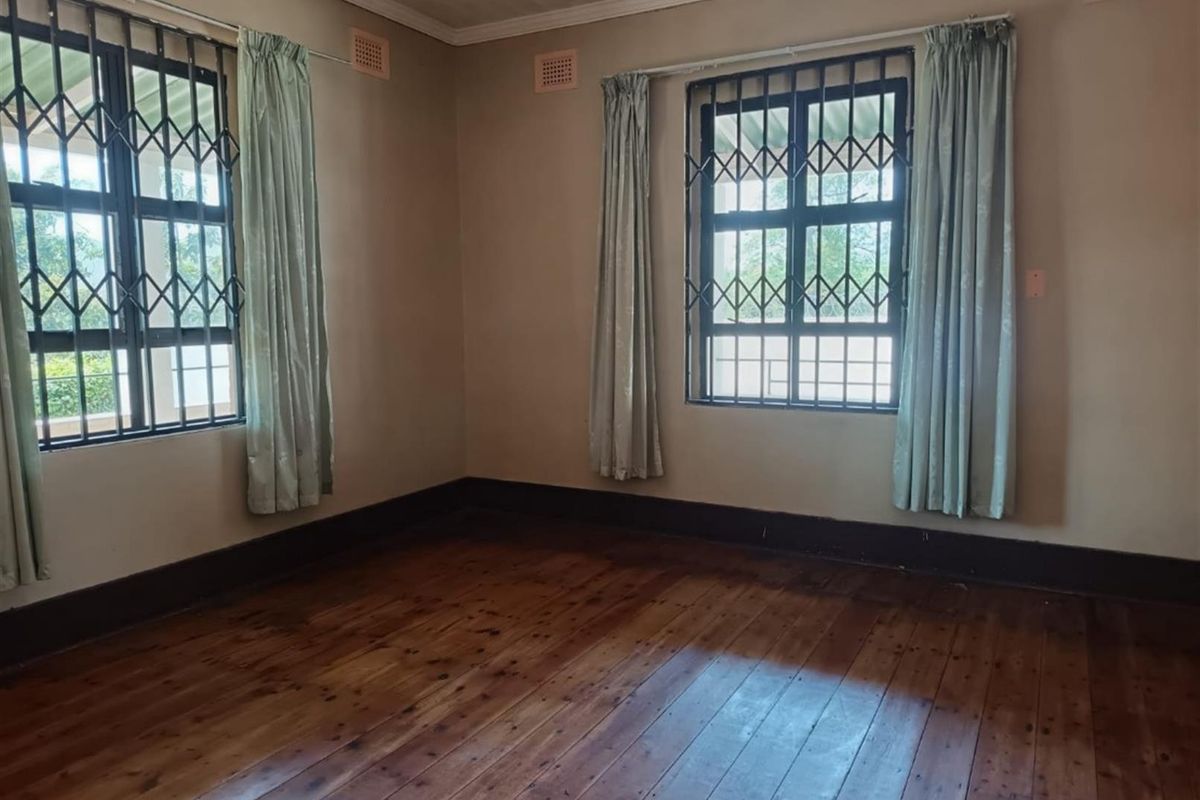 An empty bedroom featuring original timber flooring, security bars on windows, and a classic timber ceiling, offering a blank canvas for renovation.