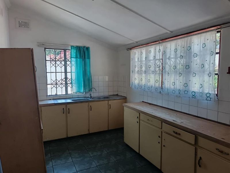 A functional kitchen featuring built-in cabinetry, a stainless steel sink, and tiled splashbacks, offering a dated aesthetic ready for modernization.
