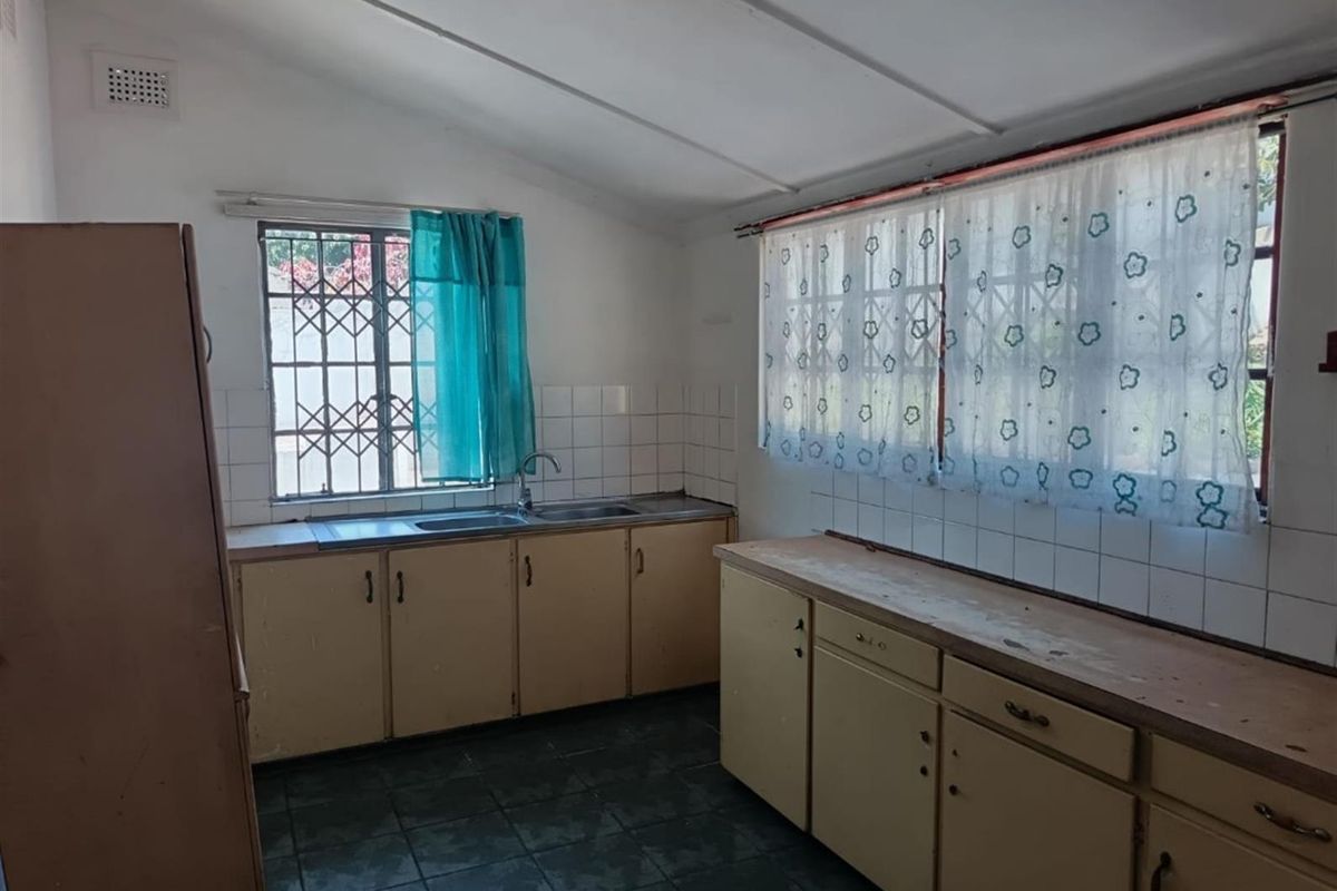 A functional kitchen featuring built-in cabinetry, a stainless steel sink, and tiled splashbacks, offering a dated aesthetic ready for modernization.