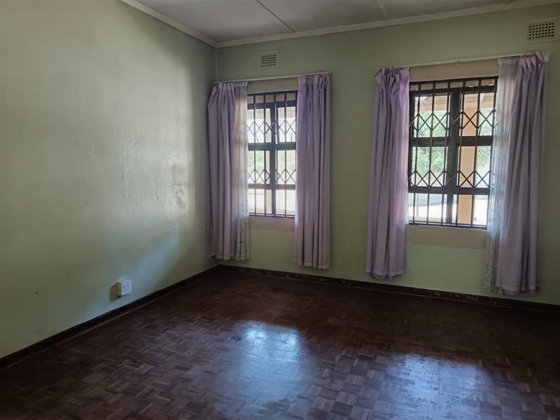 An empty bedroom featuring parquet flooring, security bars on the windows, and neutral wall paint, offering a blank canvas for renovation.