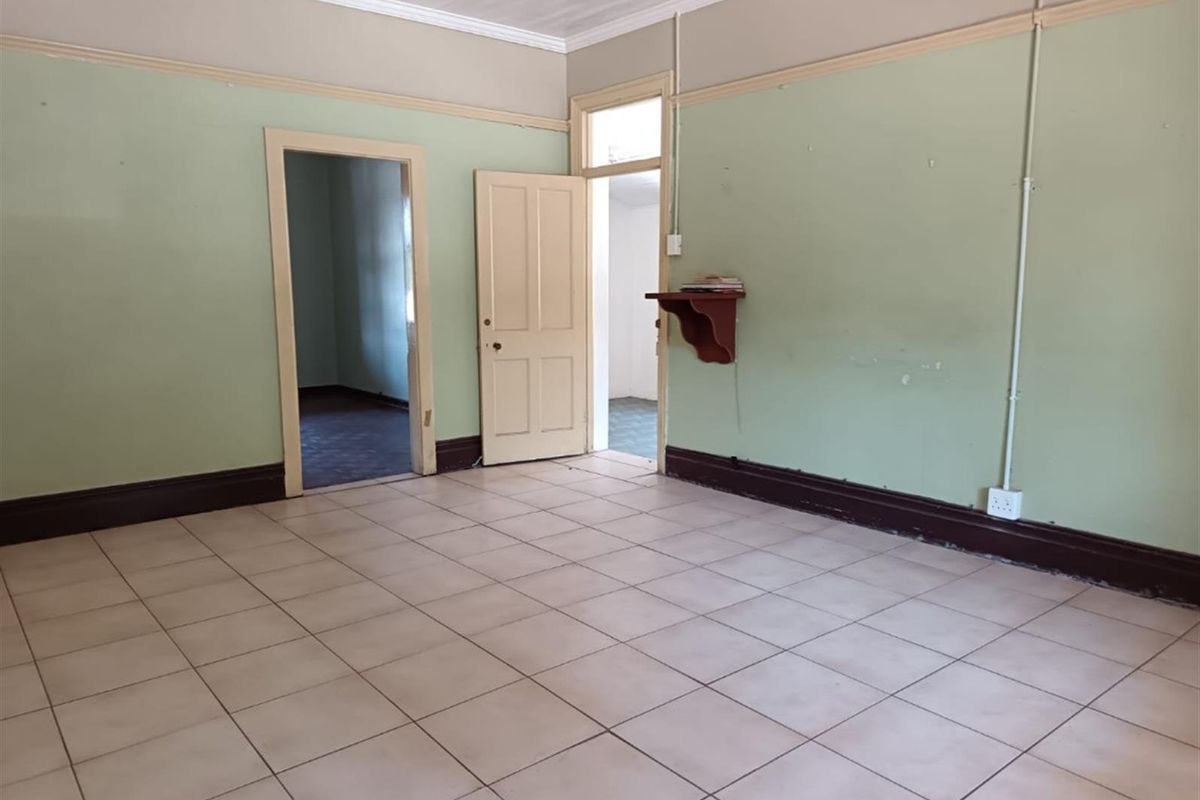 An empty living room featuring tiled flooring, picture rails, and coved ceilings, offering a blank canvas for renovation and interior design updates.