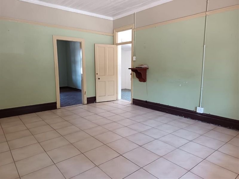An empty living room featuring tiled flooring, picture rails, and coved ceilings, offering a blank canvas for renovation and interior design updates.