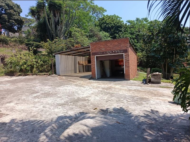 A detached brick garage featuring a roller door and an adjacent covered outdoor area with a built-in braai, set on a large concrete driveway.