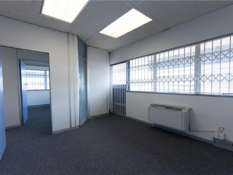A vacant office space featuring carpeted flooring, suspended ceilings with recessed lighting, and wall-mounted air conditioning, secured with window bars.