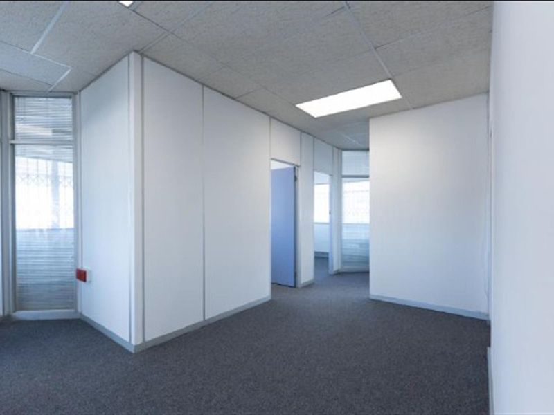 An empty office space featuring neutral partition walls, carpet flooring, and a suspended ceiling with recessed lighting.