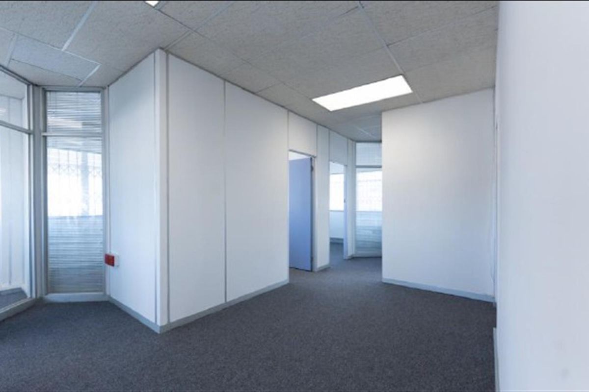 An empty office space featuring neutral partition walls, carpet flooring, and a suspended ceiling with recessed lighting.