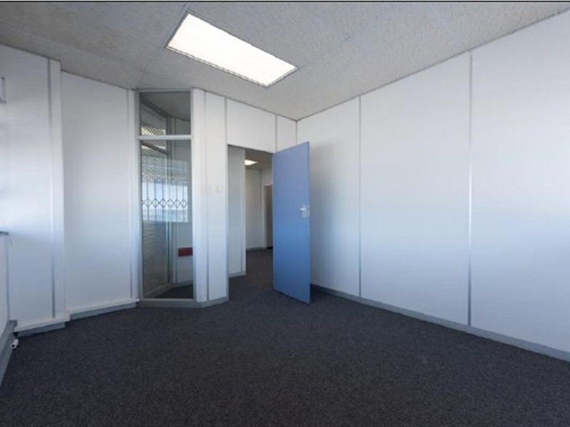 A vacant office space featuring modular partition walls, recessed ceiling lighting, and dark carpeting, providing a clean and functional professional environment.