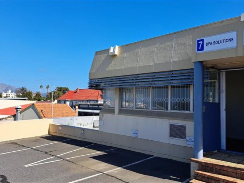 Exterior view of the office building entrance featuring a paved parking area, security bars on windows, and clear signage.