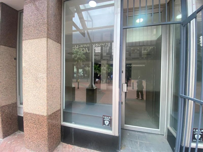 A retail storefront entrance featuring granite cladding, large glass display windows, and a secure metal gate.