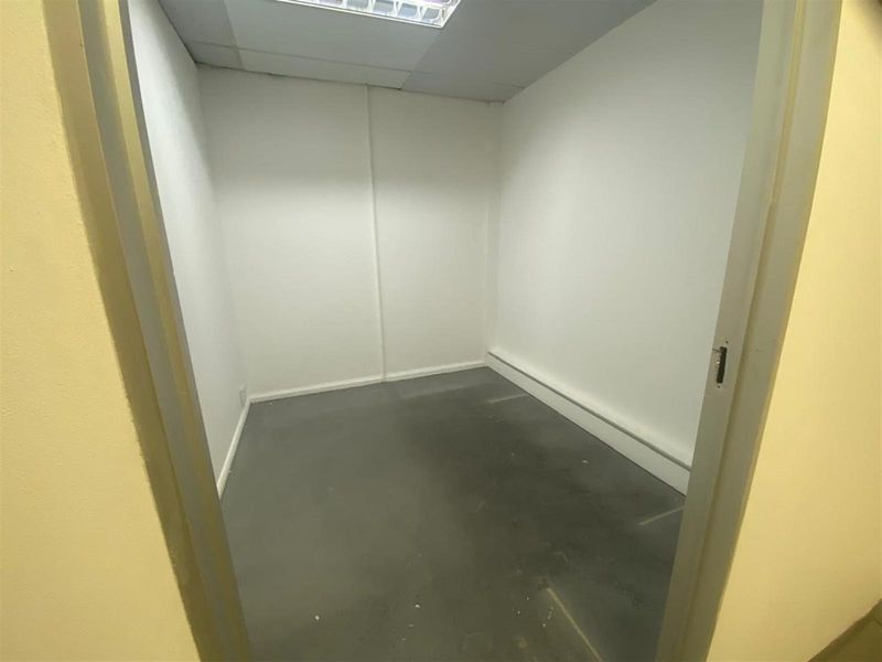 A small, empty utility or storage room featuring a suspended ceiling, recessed lighting, and plain wall finishes.