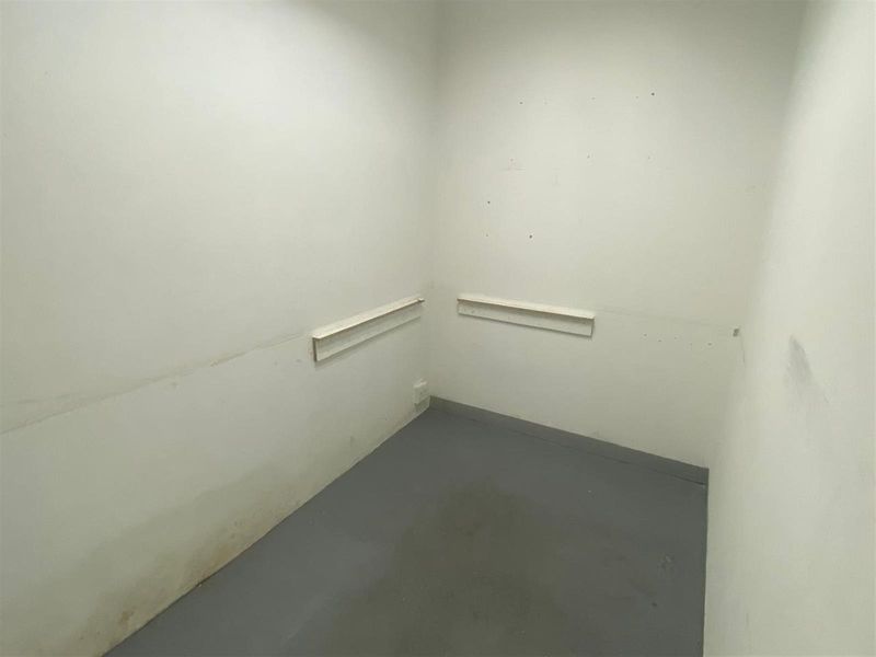 A small, empty utility or storage space featuring plain walls with mounted shelving rails and a simple floor finish.