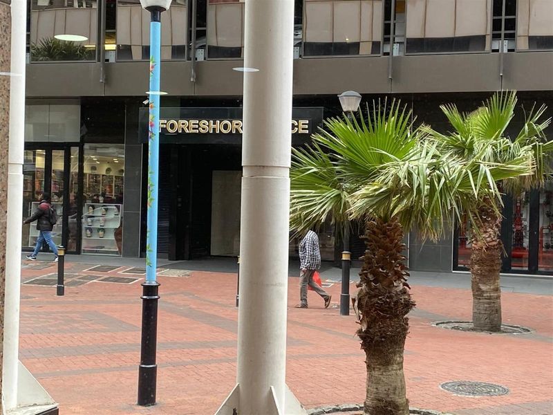 Exterior view of a commercial retail storefront featuring paved pedestrian access and structural columns in an urban setting.