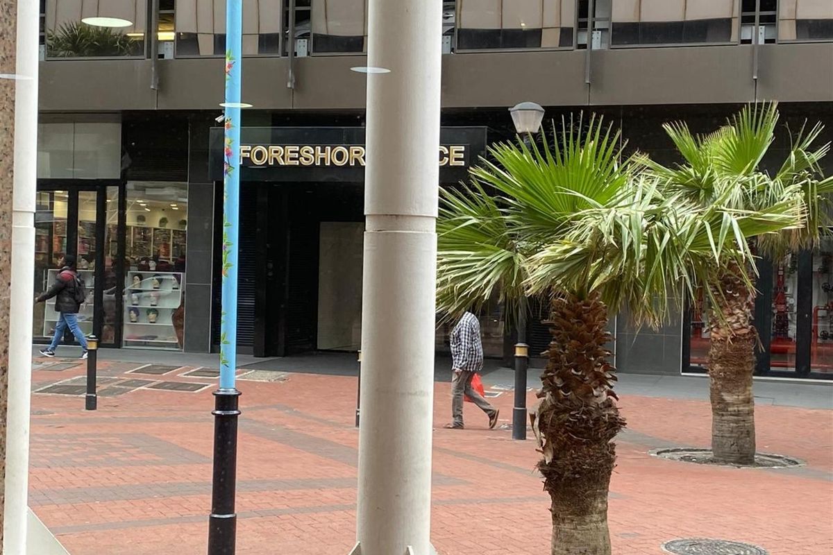 Exterior view of a commercial retail storefront featuring paved pedestrian access and structural columns in an urban setting.