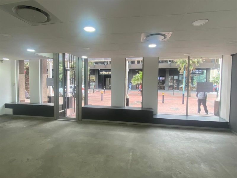 An open-plan retail space featuring large display windows, recessed lighting, and concrete flooring, offering excellent visibility for a storefront or showroom.