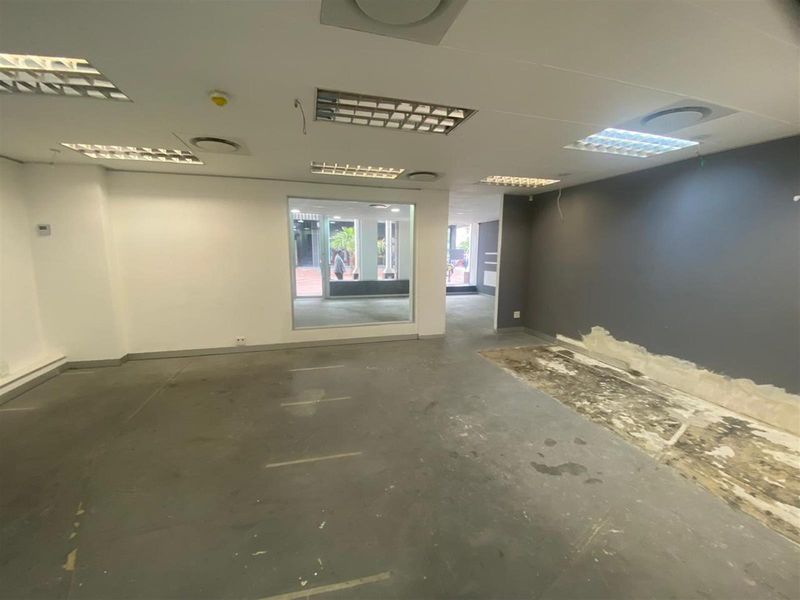 An empty, open-plan retail space featuring a large display window, recessed lighting, and exposed concrete flooring requiring refurbishment.