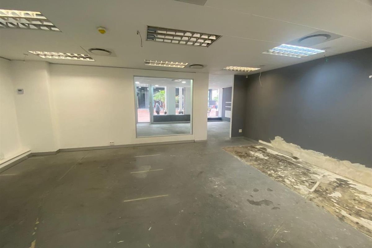 An empty, open-plan retail space featuring a large display window, recessed lighting, and exposed concrete flooring requiring refurbishment.