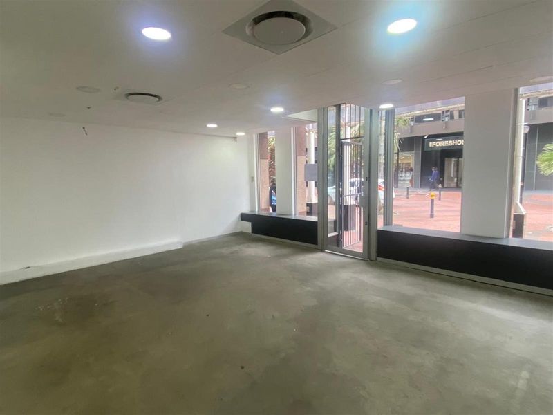 Empty retail space featuring large display windows, concrete flooring, recessed lighting, and ducted air conditioning, suitable for a variety of commercial uses.