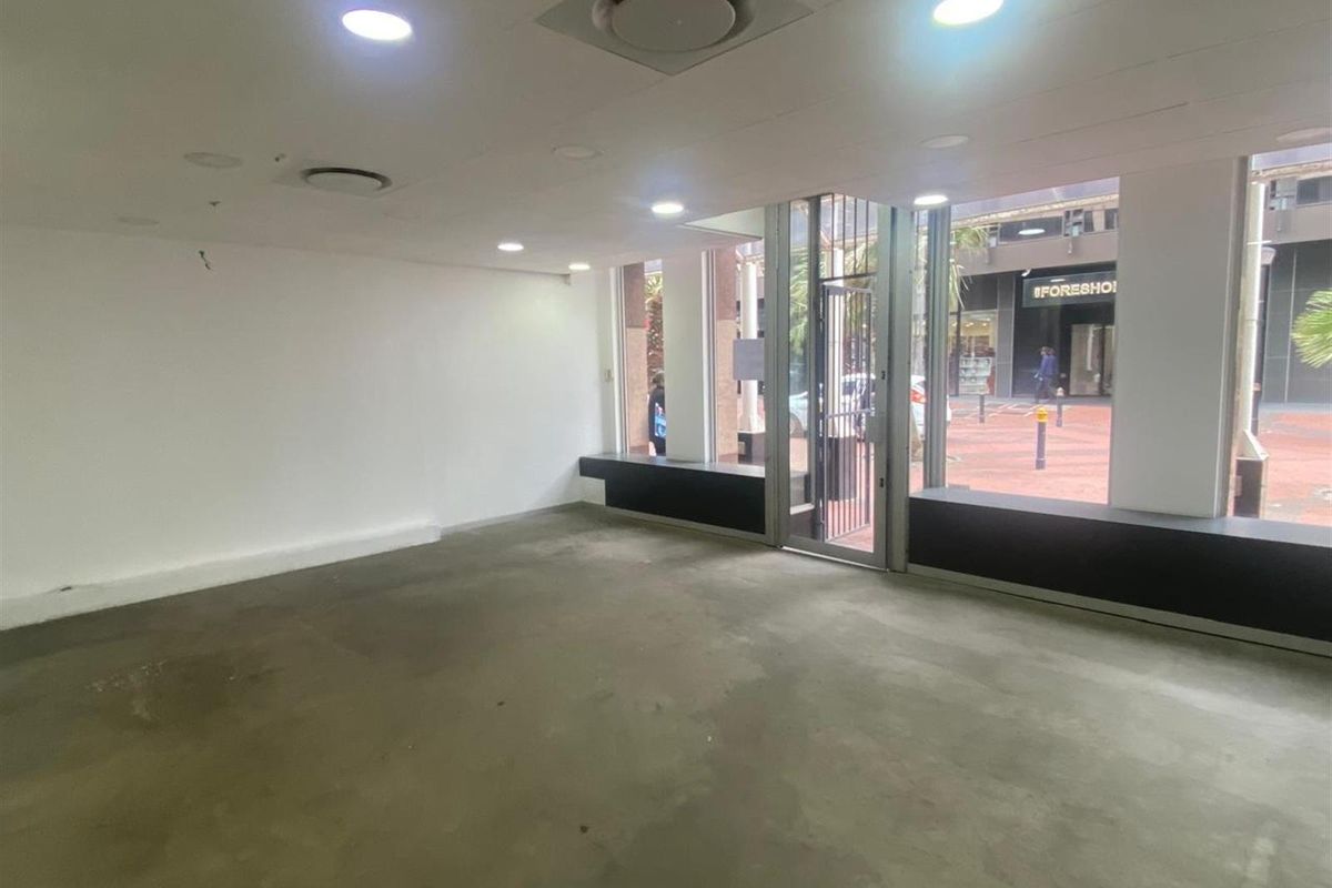 Empty retail space featuring large display windows, concrete flooring, recessed lighting, and ducted air conditioning, suitable for a variety of commercial uses.