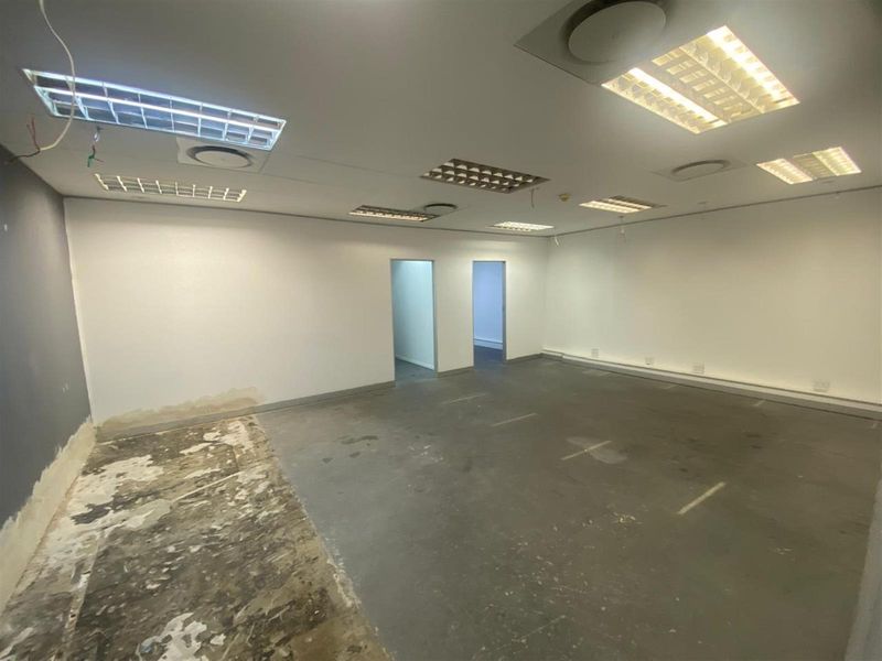 An empty, open-plan commercial space featuring a suspended ceiling with recessed lighting and unfinished concrete flooring, ready for custom fit-out.