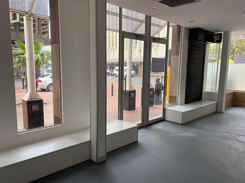Empty retail storefront featuring large glass display windows, glass entrance doors, built-in display platforms, and recessed ceiling lighting.