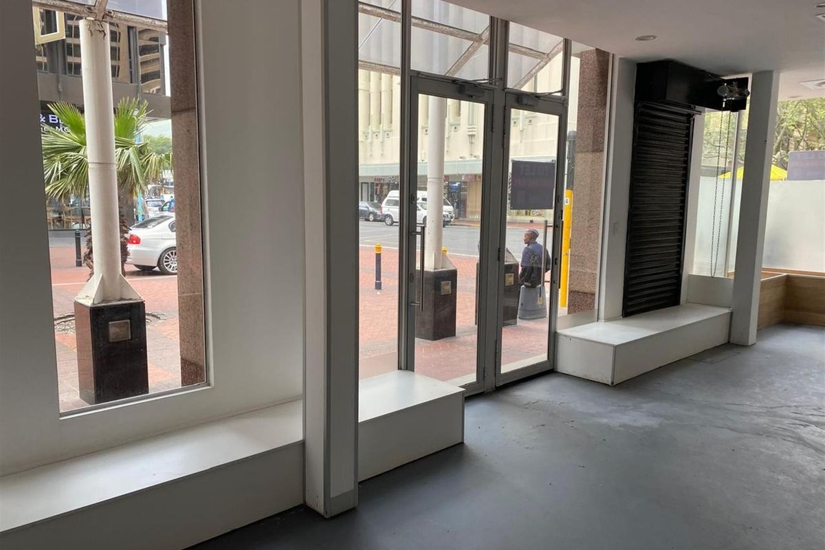 Empty retail storefront featuring large glass display windows, glass entrance doors, built-in display platforms, and recessed ceiling lighting.