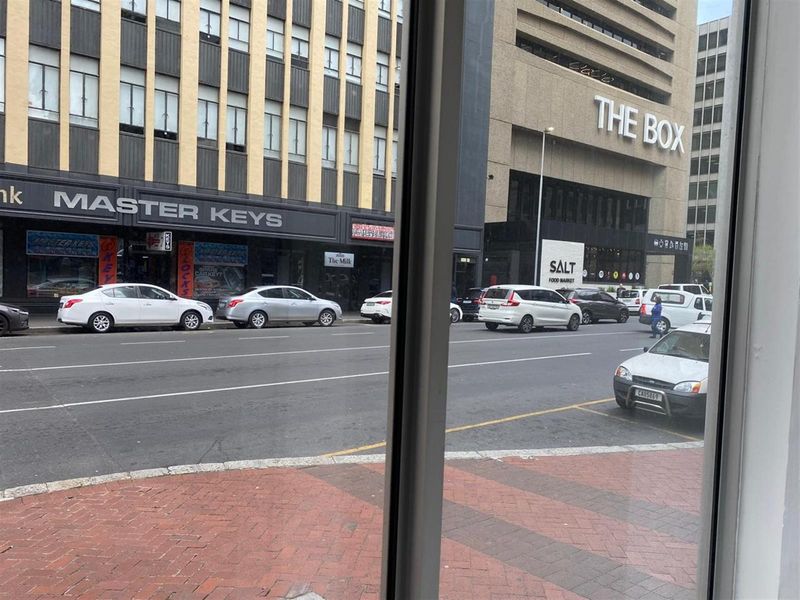 A street-level view looking out onto a busy urban road with commercial buildings and parked vehicles.