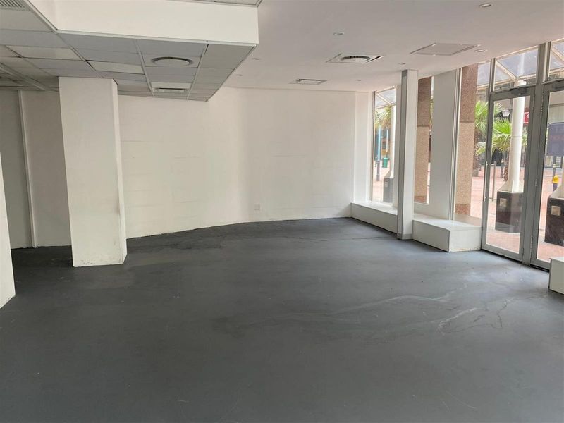 Empty open-plan retail space featuring large display windows, recessed ceiling lighting, and painted concrete flooring, suitable for a variety of commercial uses.