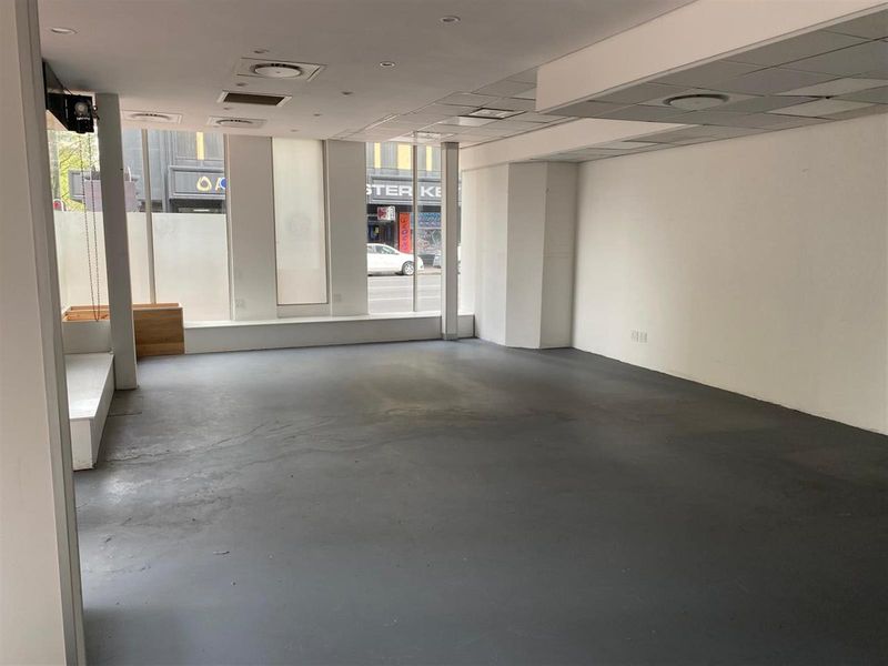 Open-plan retail space featuring large street-facing display windows, recessed lighting, and durable painted concrete flooring, suitable for various commercial business applications.