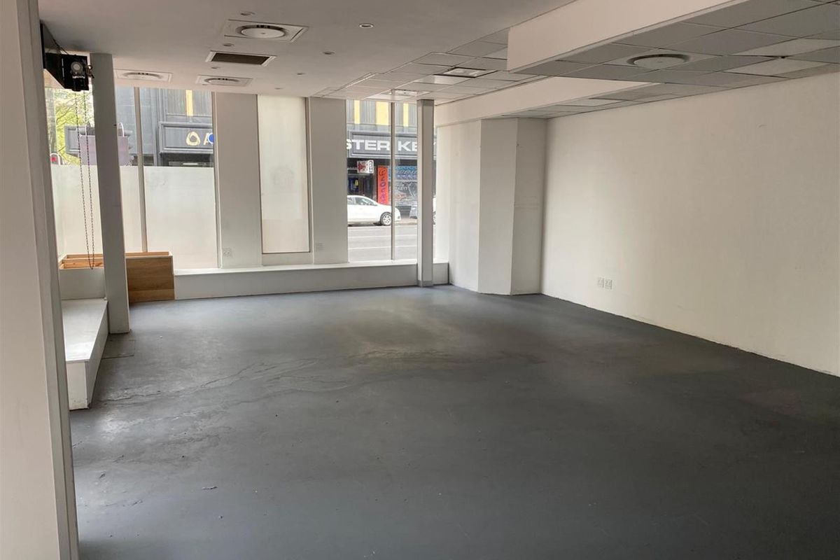 Open-plan retail space featuring large street-facing display windows, recessed lighting, and durable painted concrete flooring, suitable for various commercial business applications.