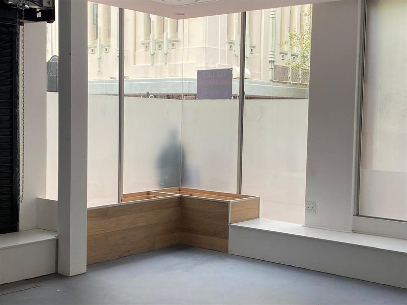 A bright, open-plan retail space featuring large corner display windows, built-in timber-look bench seating, and polished concrete flooring, ideal for a modern showroom or shop.