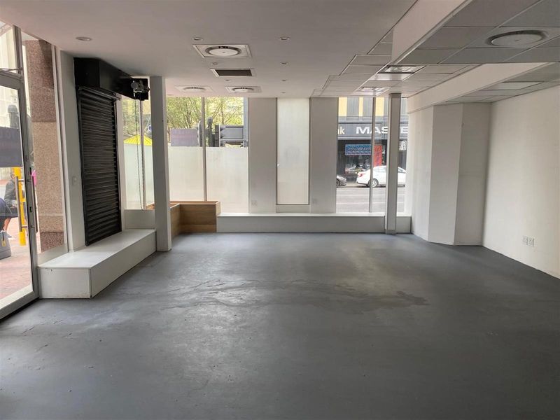 A vacant open-plan retail space featuring large display windows, concrete flooring, and recessed ceiling lighting, suitable for a variety of commercial business uses.