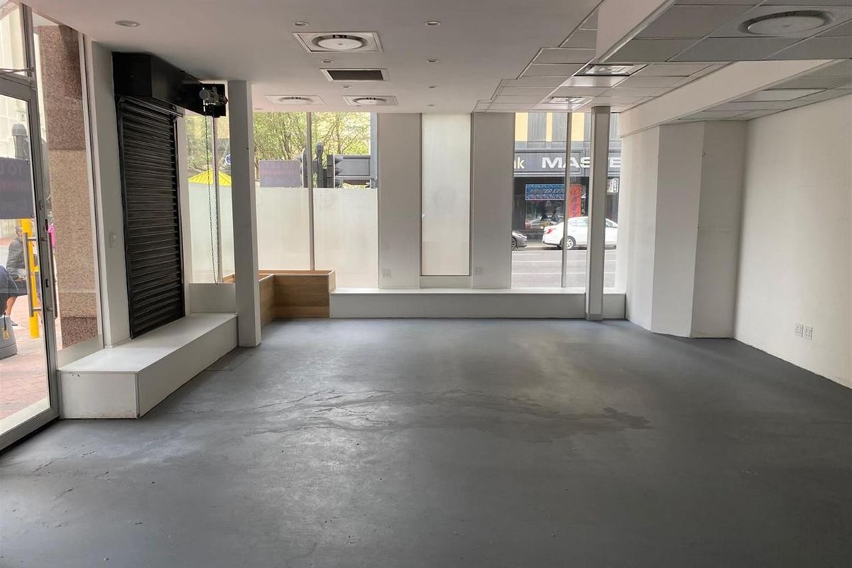 A vacant open-plan retail space featuring large display windows, concrete flooring, and recessed ceiling lighting, suitable for a variety of commercial business uses.