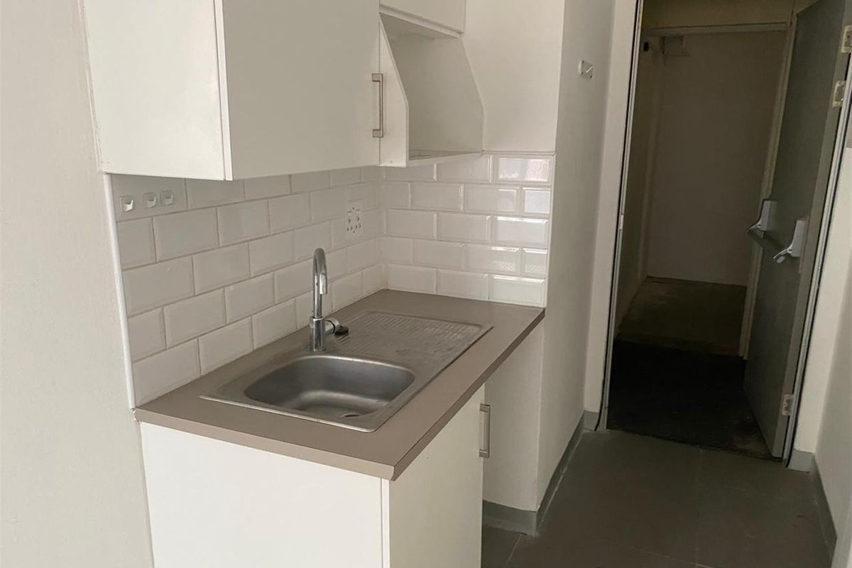 A compact kitchenette featuring white cabinetry, a stainless steel sink, and a clean subway tile backsplash.
