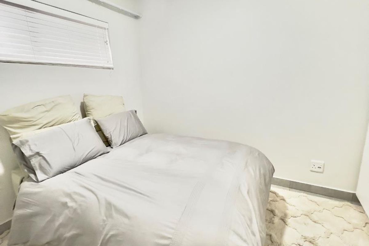 A simple bedroom featuring neutral walls, tiled flooring, and a window fitted with horizontal blinds.