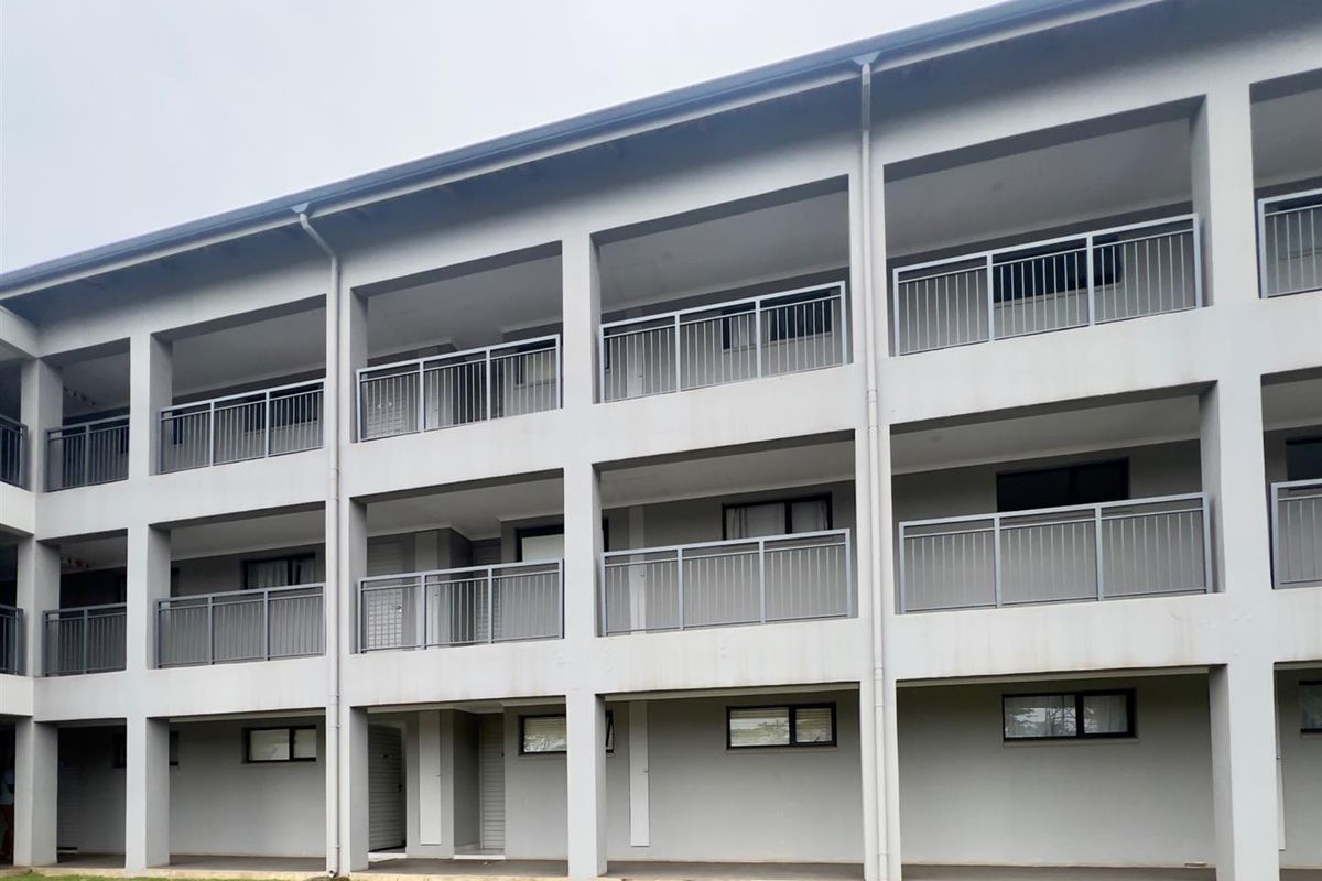 Exterior view of a multi-story apartment building featuring concrete balconies with metal railings and a ground-level walkway.