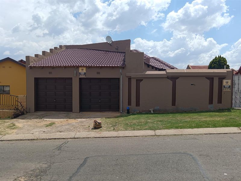 Front view of a residential property featuring a double garage with brown doors, a tiled roof, and a perimeter boundary wall.